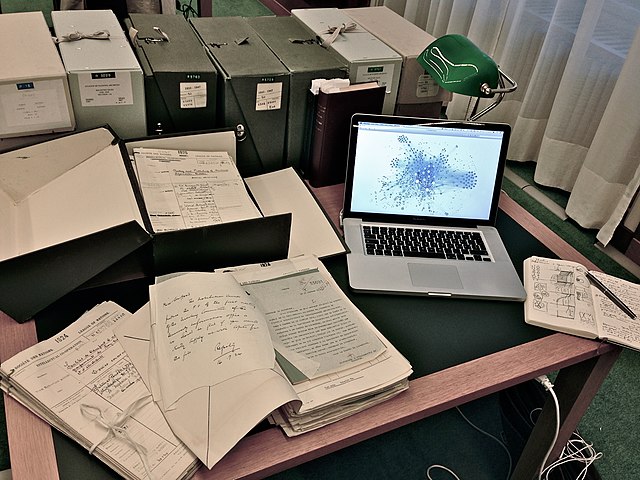 Photo of desk with papers, a laptop, and archival boxes on it.